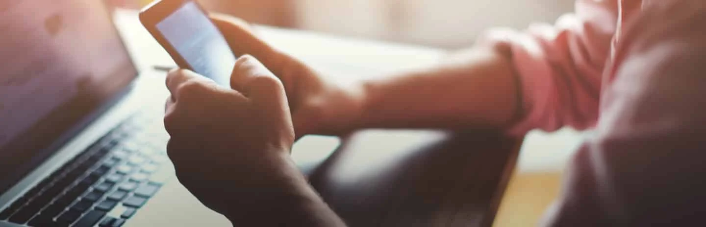 personne devant un ordinateur portable avec un téléphone entre les mains