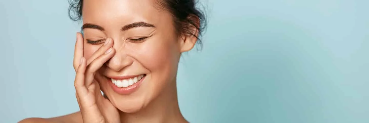 femme souriante fermant les yeux et setouchant le visage avec la main