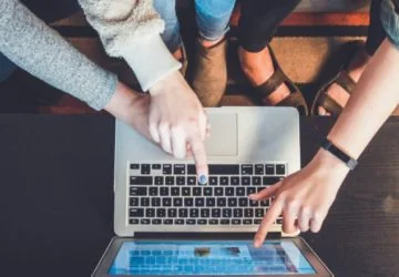 4 bras pointant vers un écran d'ordinateur portable