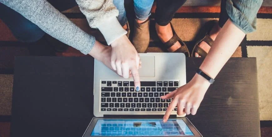 4 bras pointant vers un écran d'ordinateur portable